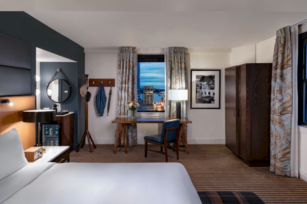 The image shows a modern, well-decorated hotel room with a bed, desk, chair, wardrobe, and a city view from the window, ending the sentence.