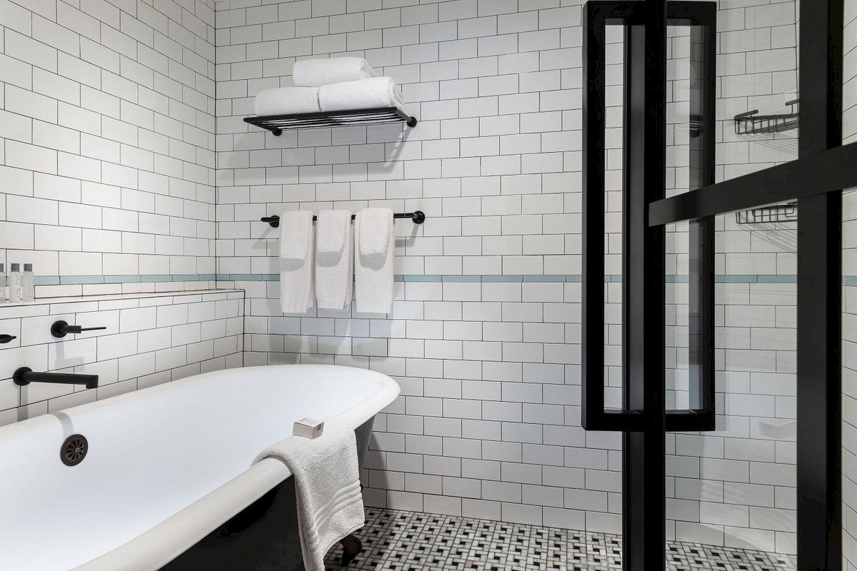 A bathroom with a white subway-tiled wall features a classic white bathtub, towels, and black metal shower door frame and fixtures.