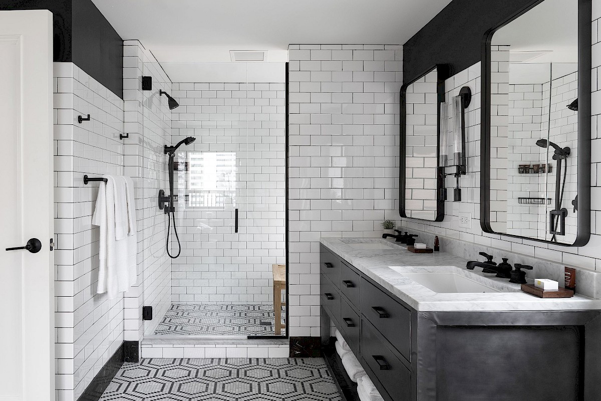 A modern bathroom with dual sinks, black fixtures, a glass shower, and white subway tiles creating a sleek, elegant design.