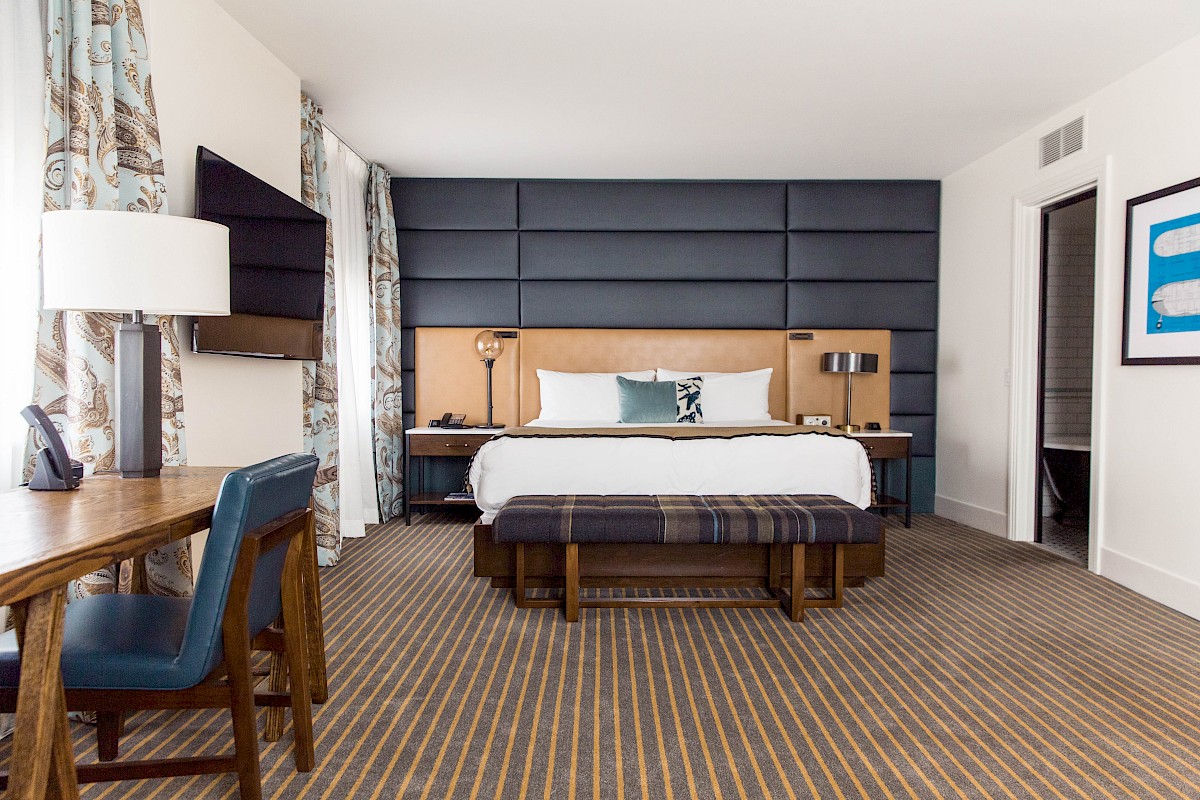 A modern hotel room with a neatly made bed, desk, chair, TV, and stylish decor in a clean, minimalistic design.
