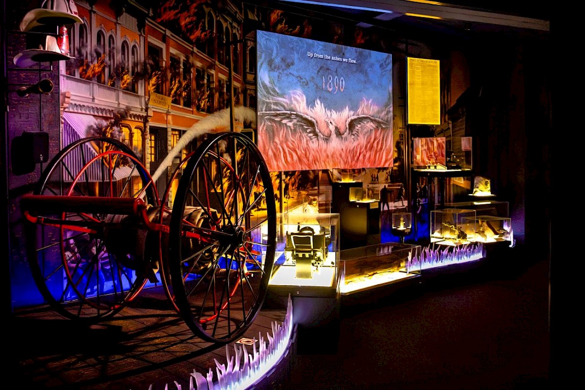 The image shows a dimly lit historical exhibit with an old cannon, artifacts, and illuminated displays, featuring a large painting in the background.