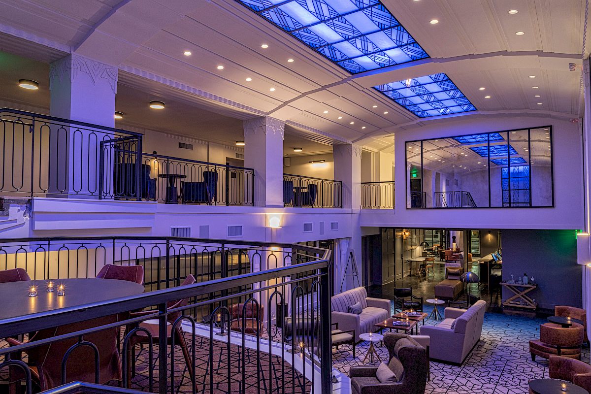 A modern, multi-level lounge area with seating, tables, and blue-lit ceiling panels. The decor is upscale with a mix of cozy and elegant touches.