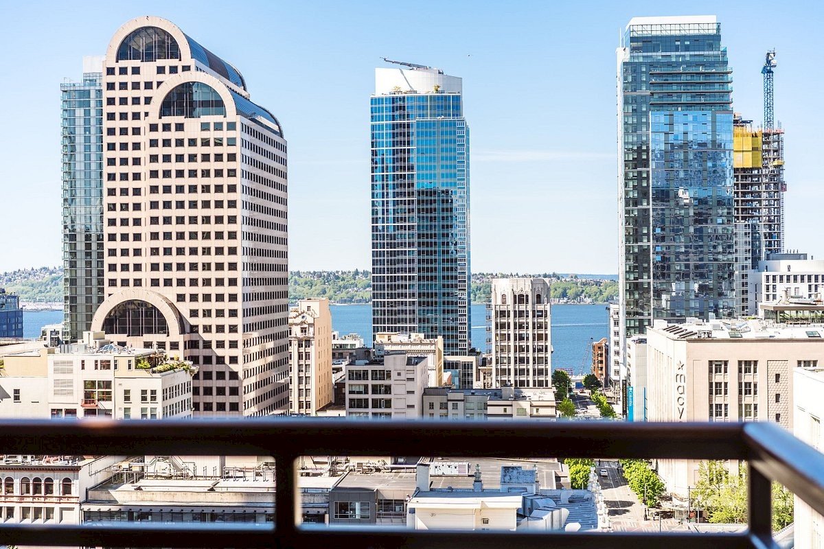 A city skyline with modern glass towers viewed from a balcony, overlooking roads and water in the distance.