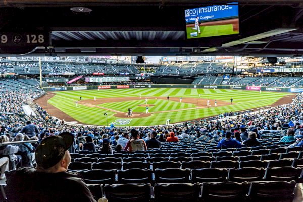 A baseball game is underway in a stadium with spectators in the stands and a digital screen displaying information, ending the sentence.