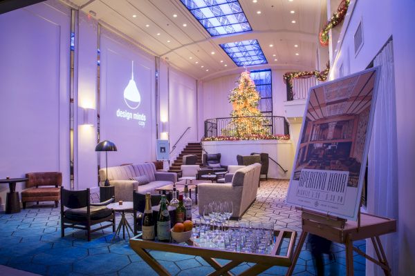 A festive, modern lounge featuring a decorated Christmas tree, comfortable seating, a refreshments cart, and a design presentation area.