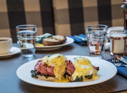 A plated Eggs Benedict dish with two glasses of water, coffee cup, and utensils on a table in a restaurant setting, ending the sentence.