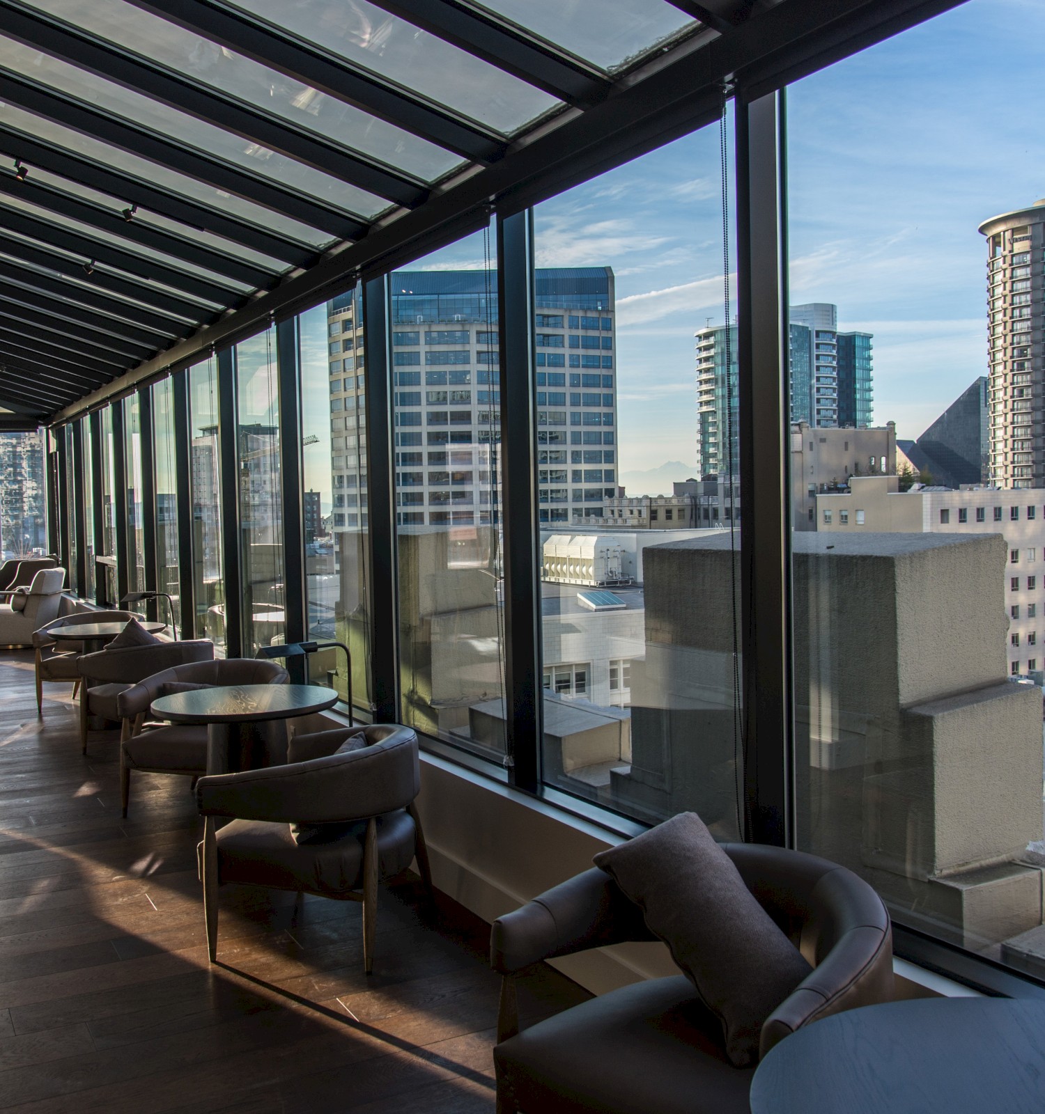 A modern indoor seating area with floor-to-ceiling windows overlooks a cityscape with high-rise buildings on a sunny day.
