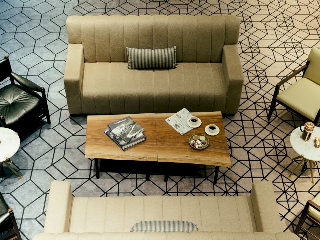 A modern living room with beige sofas, patterned carpet, wooden coffee table, magazines, and snacks, viewed from above.