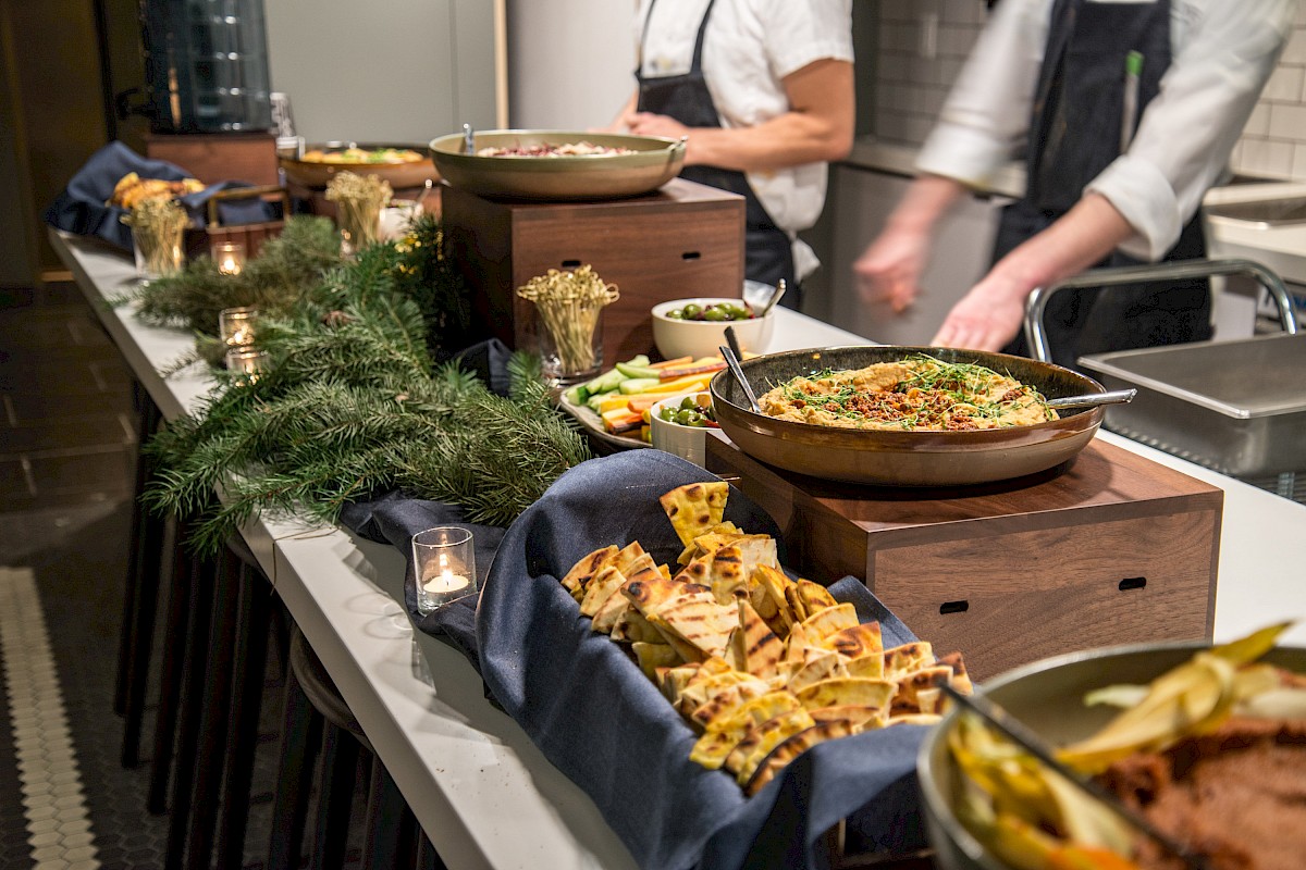 A buffet table featuring various dishes such as flatbread, salads, and cooked meals, adorned with greenery and attended by chefs.