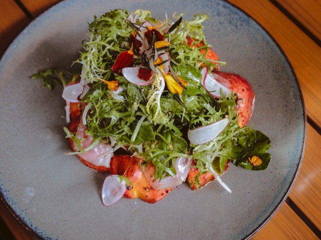 The image shows a plate of salad topped with leafy greens, radish slices, and edible flowers on a wooden table.