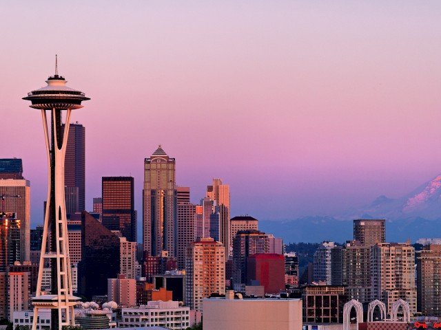 The image shows the Seattle skyline with the Space Needle prominently in the foreground and Mount Rainier visible in the background during sunset.