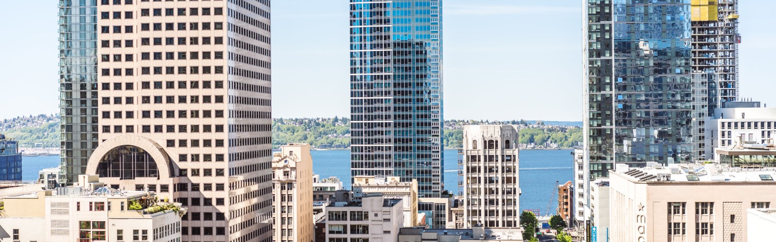 A cityscape view featuring modern skyscrapers with glass facades and a body of water in the background, seen from a balcony.