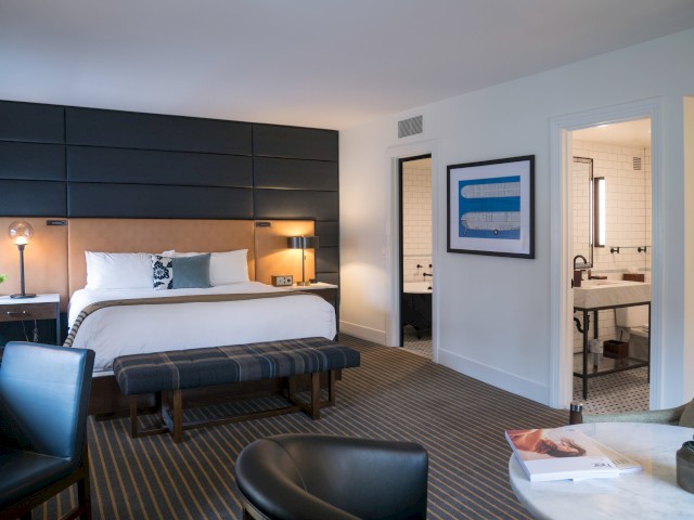 A modern hotel room with a large bed, seating area, desk, and a view into a bathroom. Parisian tile details enhance the ambiance.