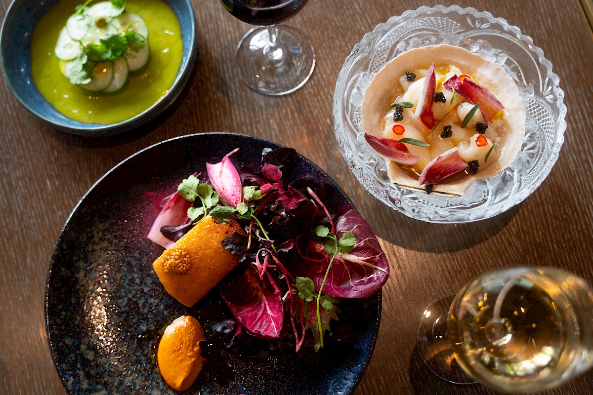 A beautifully arranged meal with dishes of salad, vegetables, and red wine. The vibrant colors and elegant presentation stand out.