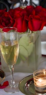 A table set with champagne glasses, red roses, candles, and rose petals, creating a romantic and elegant atmosphere.