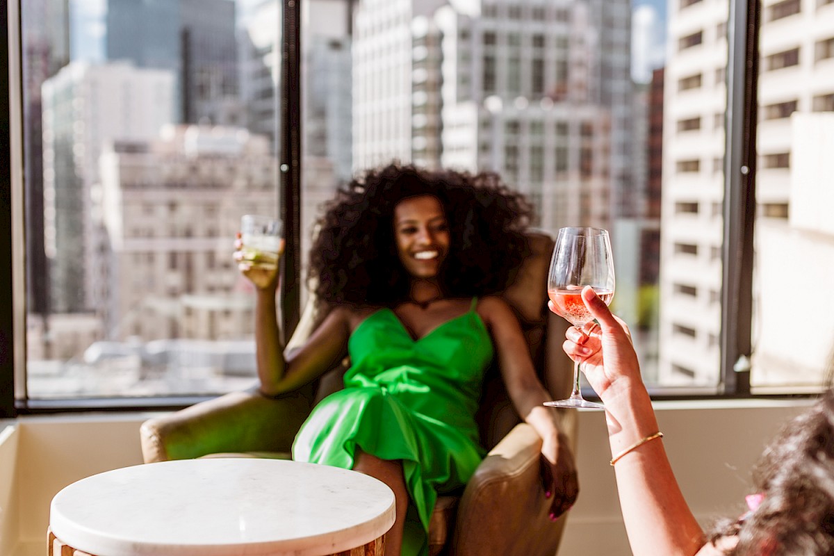 Two people are enjoying drinks in a city setting, with one person in focus wearing a green dress.