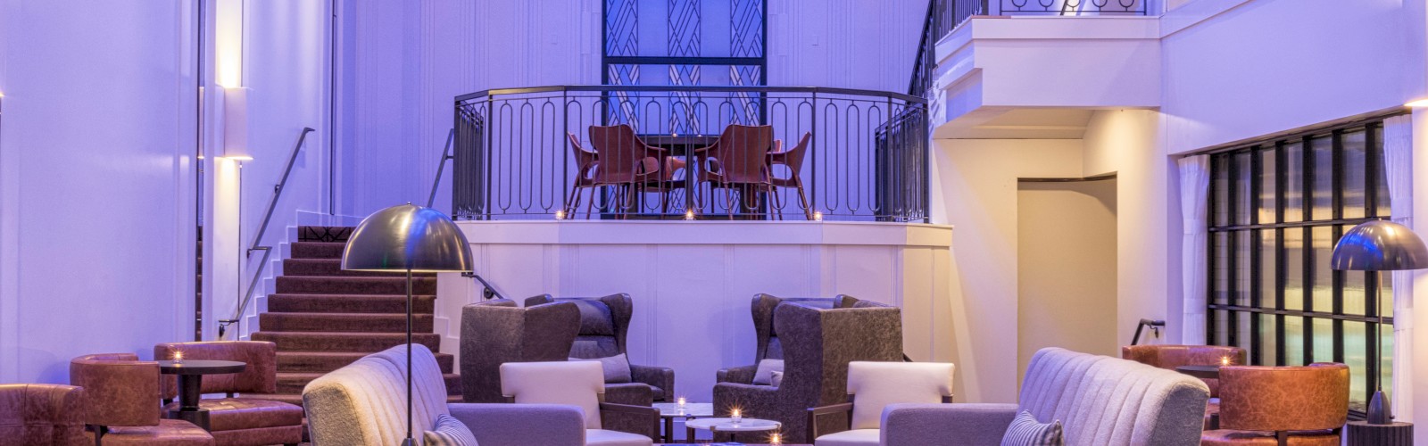 A modern, spacious lounge with various seating areas, contemporary furniture, and a mezzanine floor under ambient lighting.