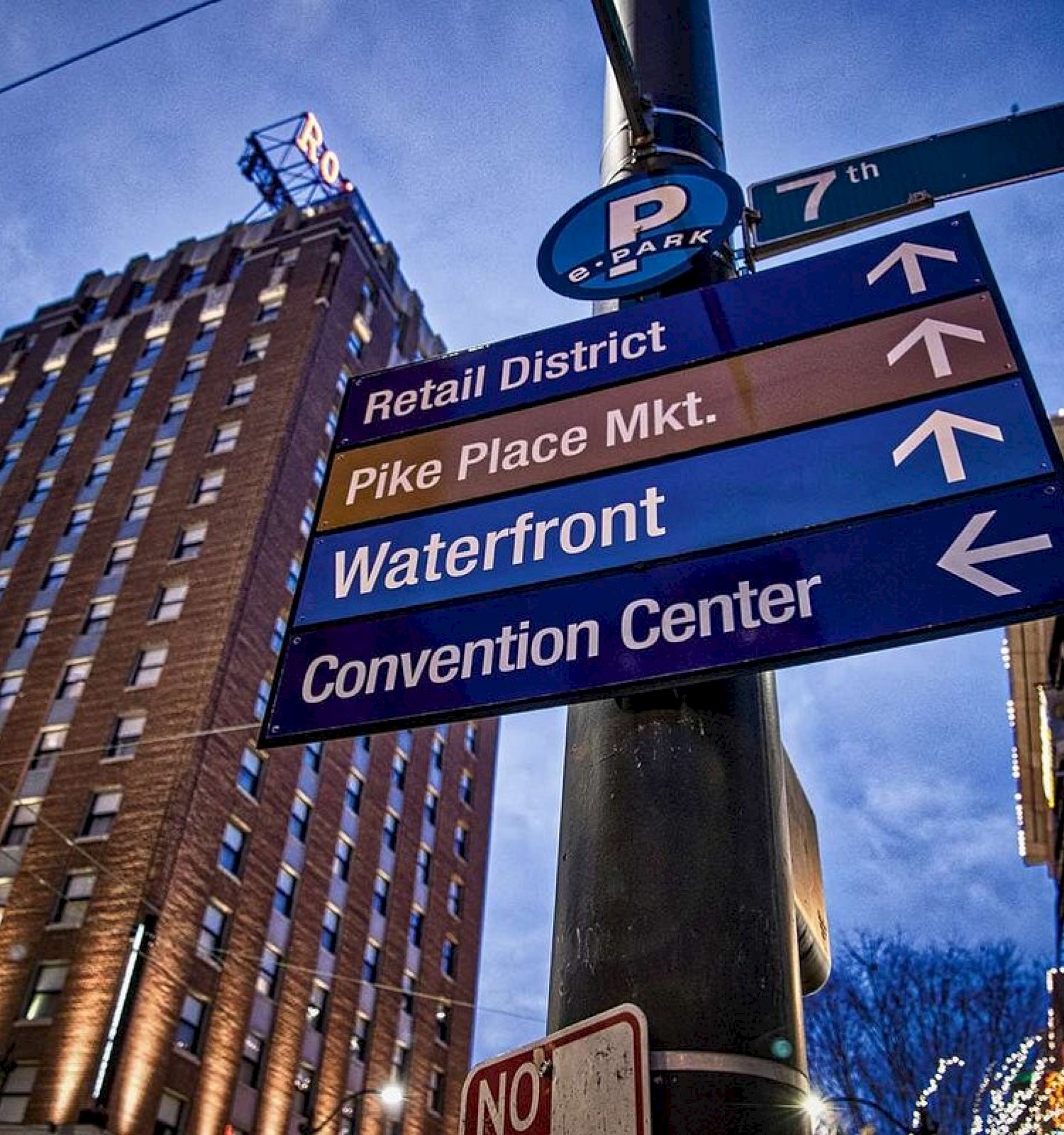 The image shows street signs pointing to the Retail District, Pike Place Market, Waterfront, and Convention Center in an urban setting.