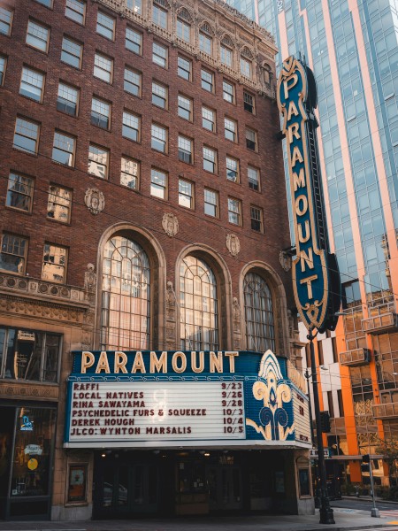 The image shows the exterior of the Paramount theater, with a marquee displaying showtimes and the iconic vertical sign on a city street.