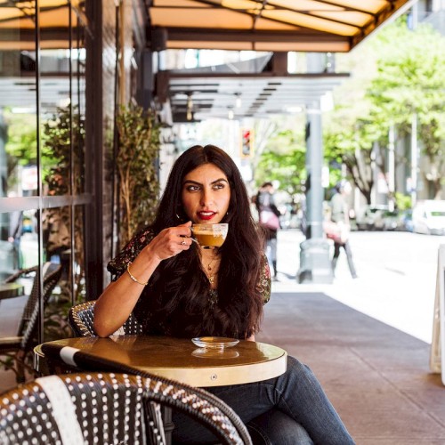A person sits at an outdoor café, sipping coffee and enjoying the city view on a sunny day.
