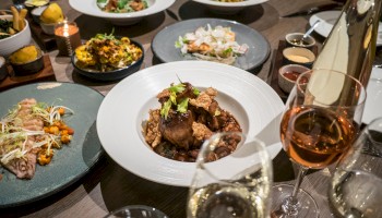 A variety of gourmet dishes are served on a table, accompanied by glasses of wine, showcasing a fine dining experience.