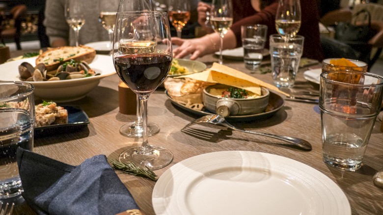 A dining table is set with plates, glasses of wine, water, and various dishes of food, with people sitting around enjoying the meal.