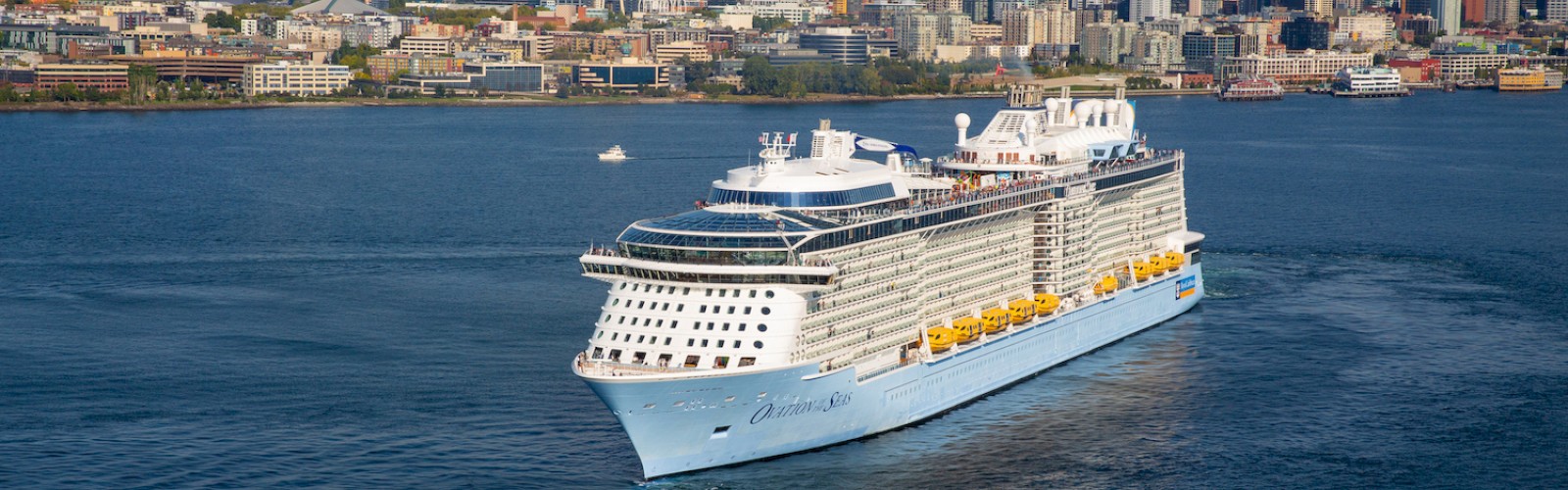 A large white cruise ship sails near a city skyline with tall buildings and a waterfront, calm blue sea, clear sky.