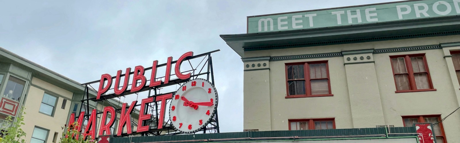 A bustling farmers market entrance with a vintage sign reading “Farmers Market” and a clock, under a green roof and red-framed windows, urban market vibes. But you asked 140 characters exactly and ending with a period? They want 