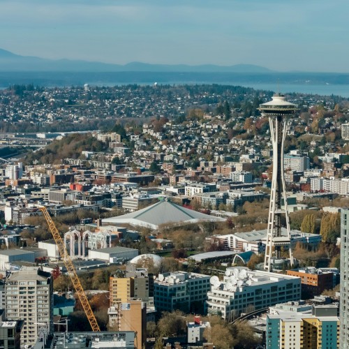 A cityscape with the Seattle-like Space Needle-style tower, dense buildings, and a distant water view under a cloudy sky.