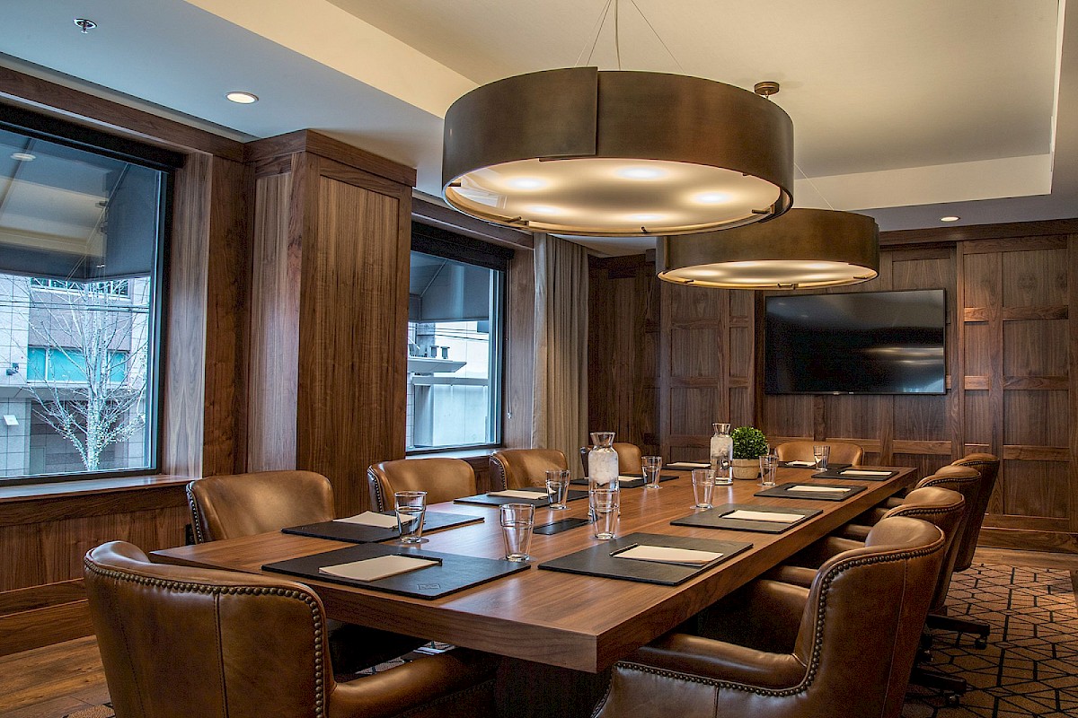 A formal conference room with a long wooden table, leather chairs, large pendant lights, and windowed walls. 140 characters, ending the sentence.