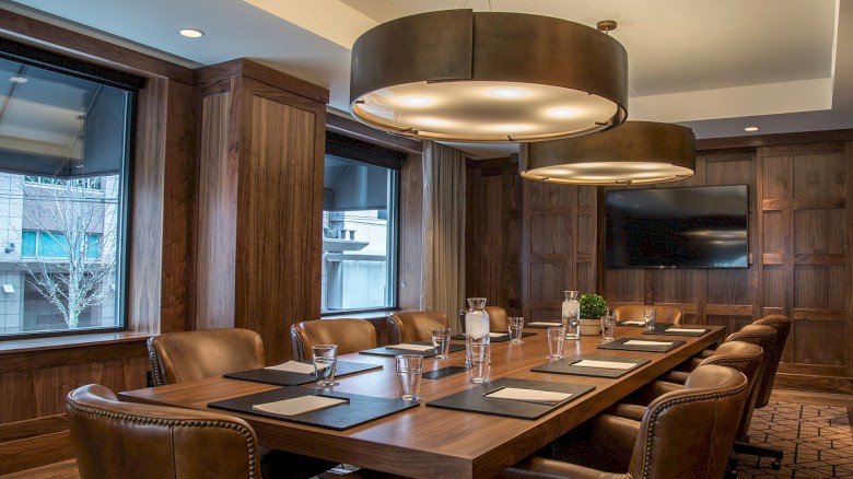 A formal conference room with a long wooden table, leather chairs, large pendant lights, and windowed walls. 140 characters, ending the sentence.