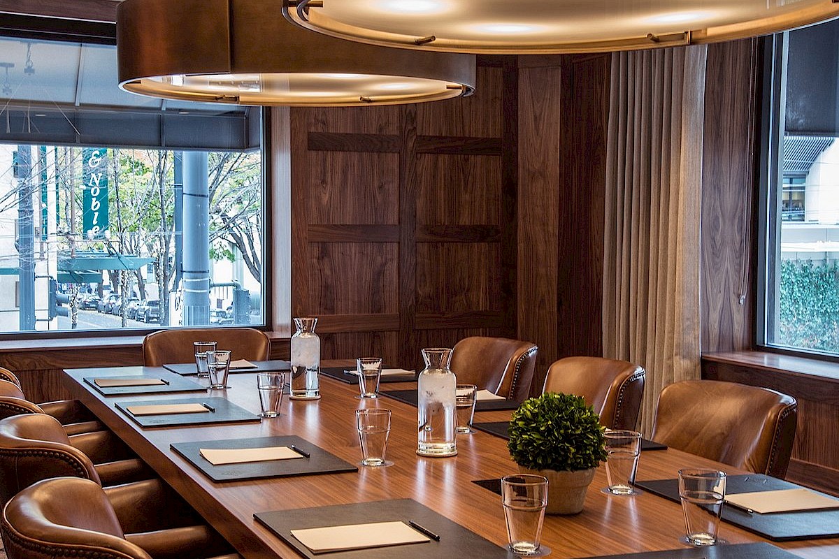 A modern conference room with a long wooden table, leather chairs, large windows, and stylish pendant lighting, ready for meetings.