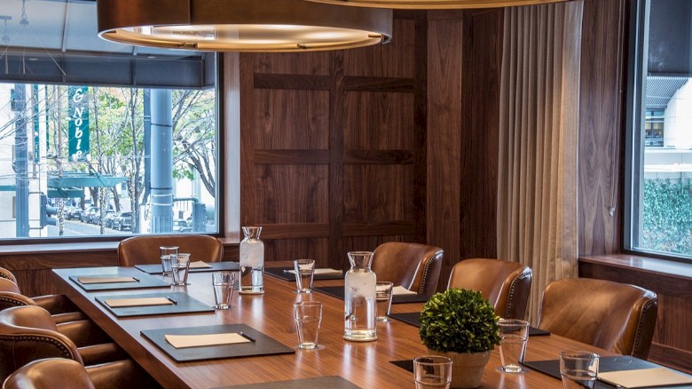 A modern conference room with a long wooden table, leather chairs, large windows, and stylish pendant lighting, ready for meetings.