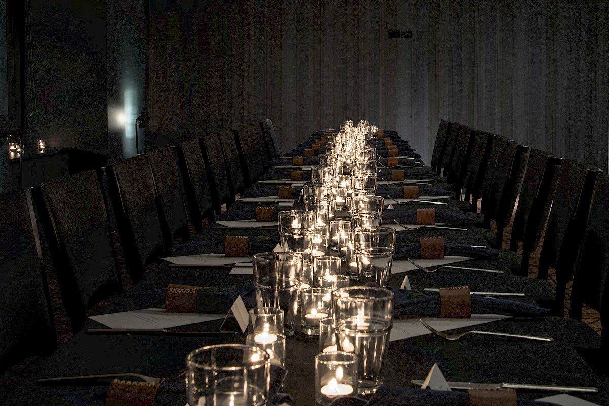 A long dining table set for a formal event, with candles, glassware, and place settings along both sides in a dim, intimate room.