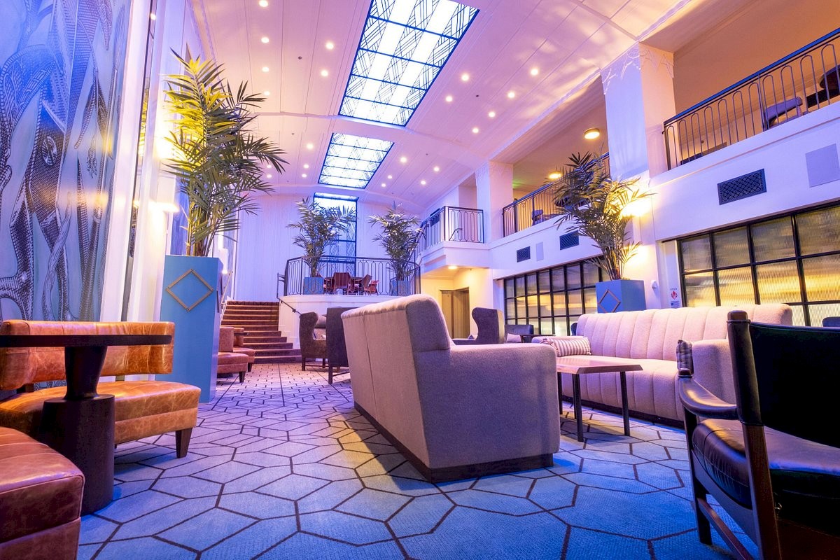 A modern hotel lobby with blue carpeting, plush seating, potted plants, and high ceilings; warm lighting and a welcoming, airy vibe.