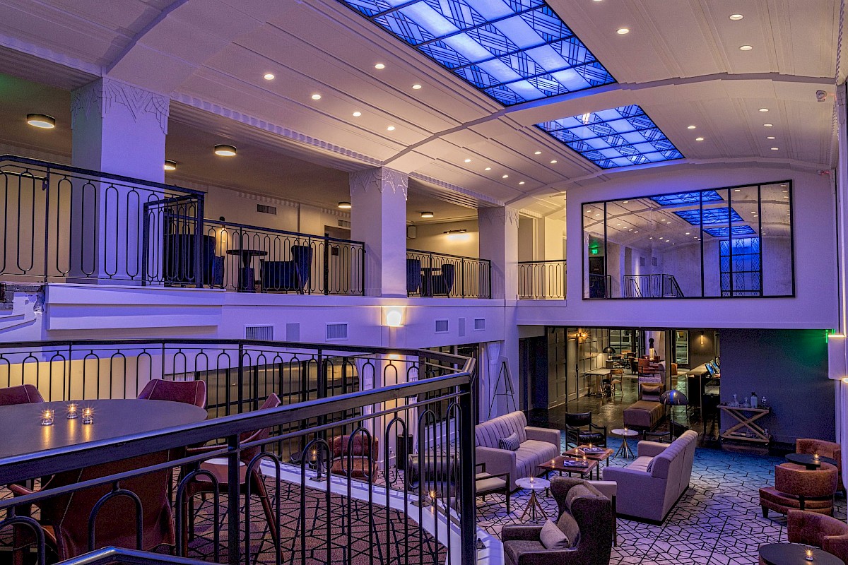 A stylish, modern hotel lobby with a mezzanine, blue accent lighting, and cozy seating areas on multiple levels.