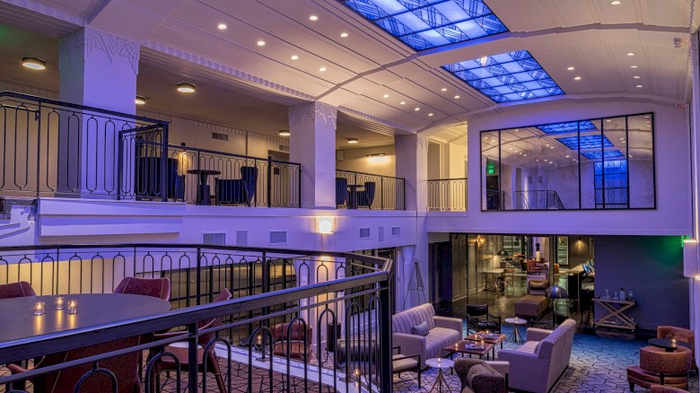 A stylish, modern hotel lobby with a mezzanine, blue accent lighting, and cozy seating areas on multiple levels.