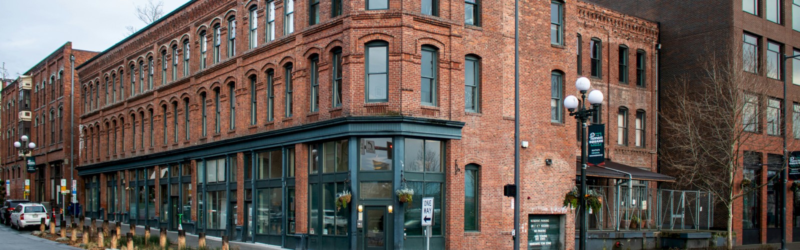 A red brick corner building with large storefront windows on the ground floor, set on a street with crosswalks and neighboring structures, coffee shop vibe.