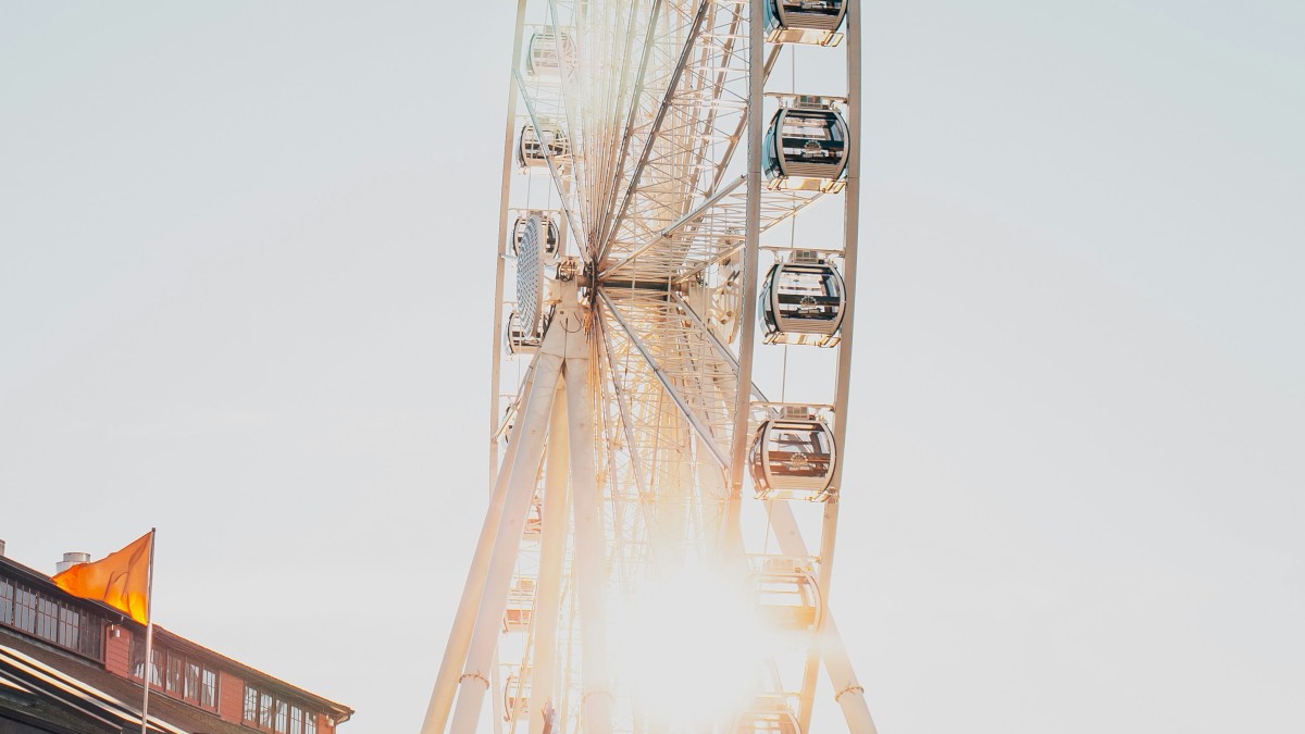 A towering Ferris wheel shines at sunset, casting warm light over the boardwalk and bustling stalls below.