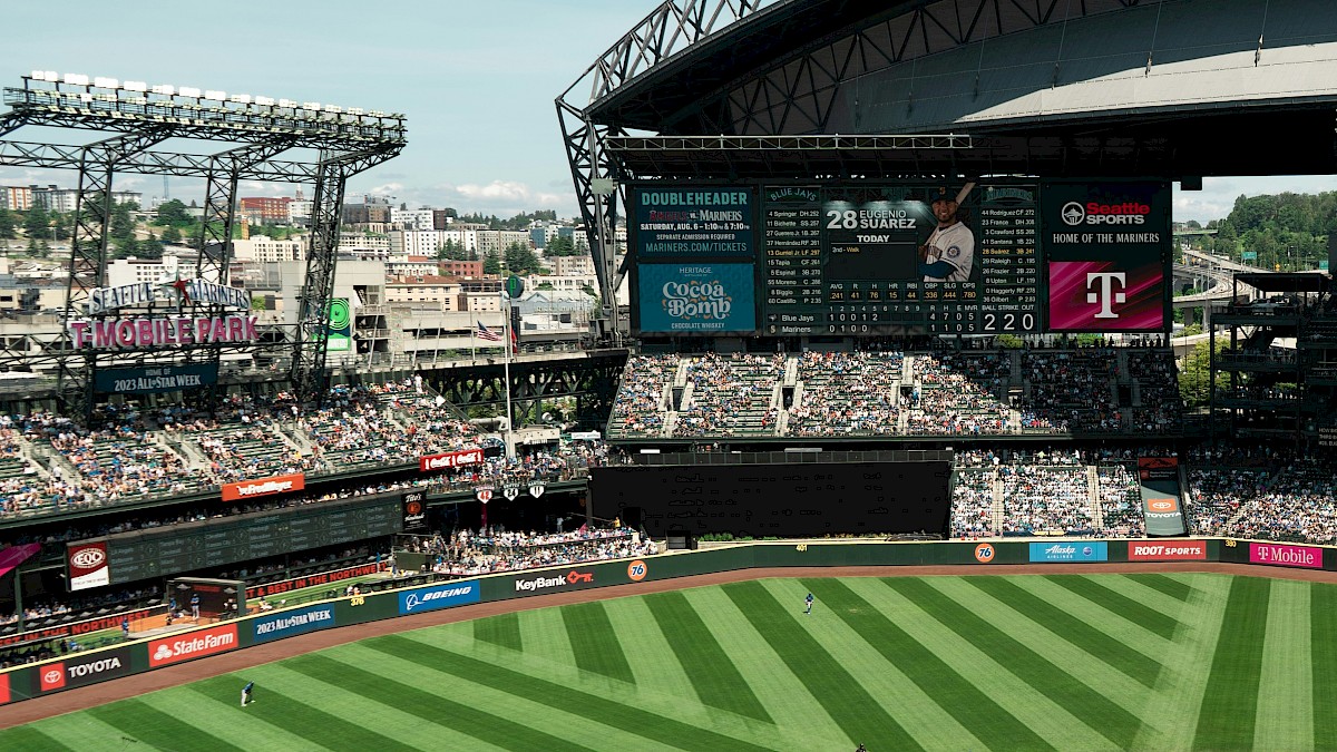A baseball stadium full of fans with a lush green field, pitch, and scoreboard under a domed roof, ready for a game.